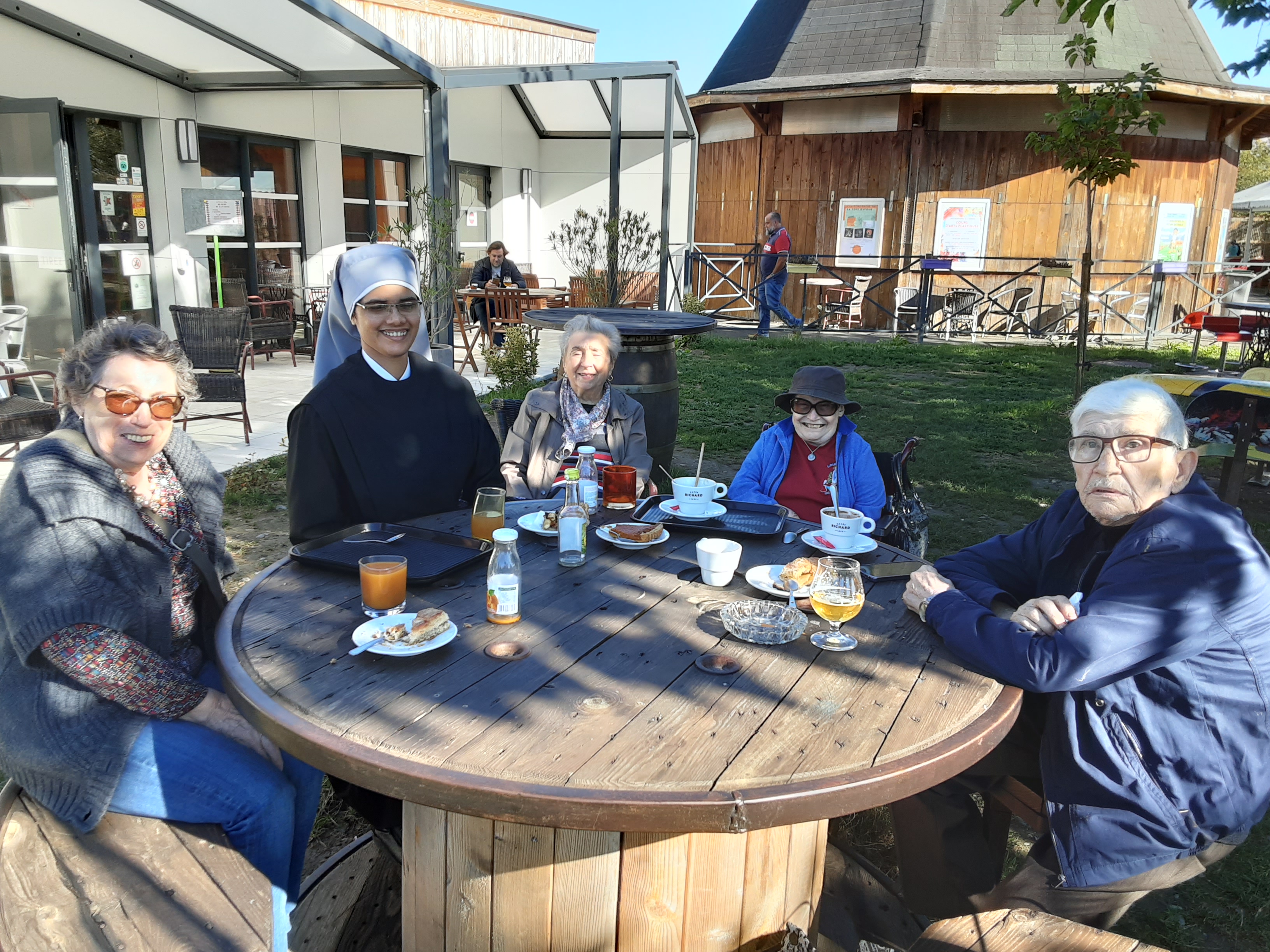 personnes âgées et petites soeurs des pauvres dans un jardin en train de boire un jus